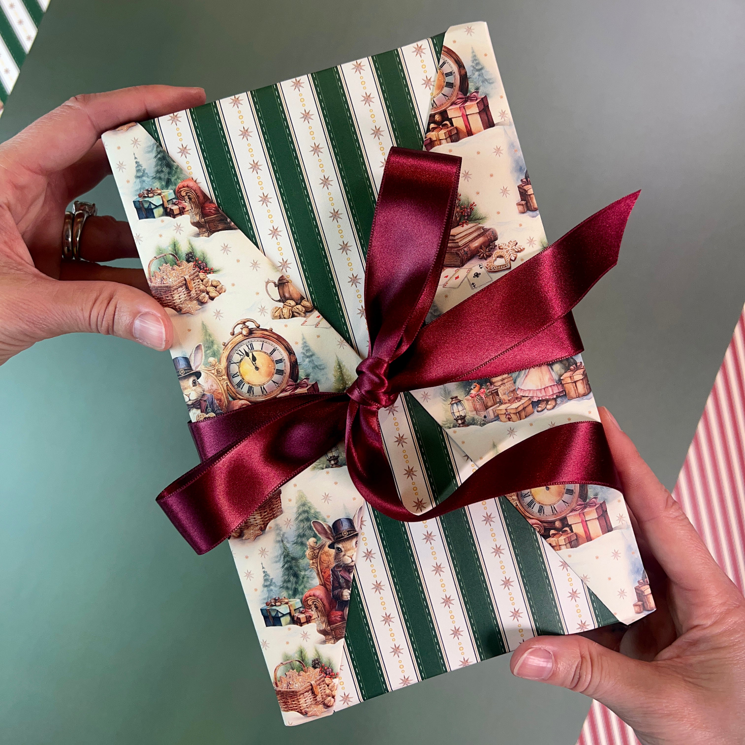 Gift box with festive design and red ribbon held by hands against a neutral background