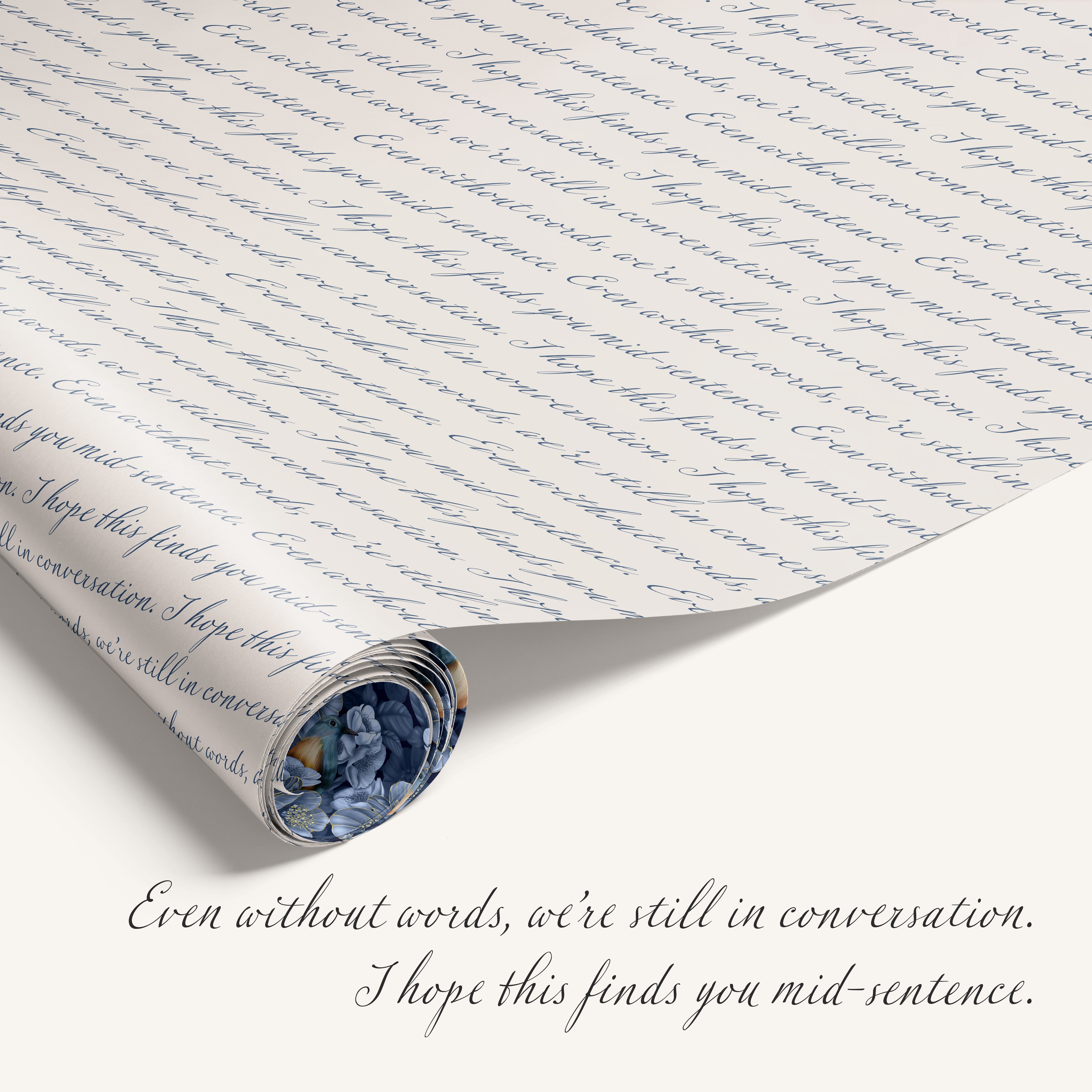 Rolled sheet of script-patterned wrapping paper beside handwritten text that reads ‘Even without words, we’re still in conversation. I hope this finds you mid-sentence.'
