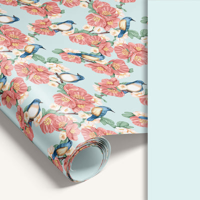 Roll of floral wrapping paper with pink flowers and blue birds on a light blue background.