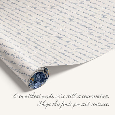 Rolled sheet of script-patterned wrapping paper beside handwritten text that reads ‘Even without words, we’re still in conversation. I hope this finds you mid-sentence.'